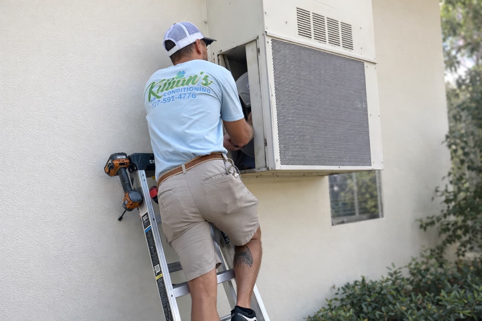 Killian's Air Conditioning technician servicing an outdoor AC unit on a ladder in St. Petersburg